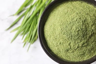 Photo of Wheat grass powder in bowl on white table, top view. Space for text