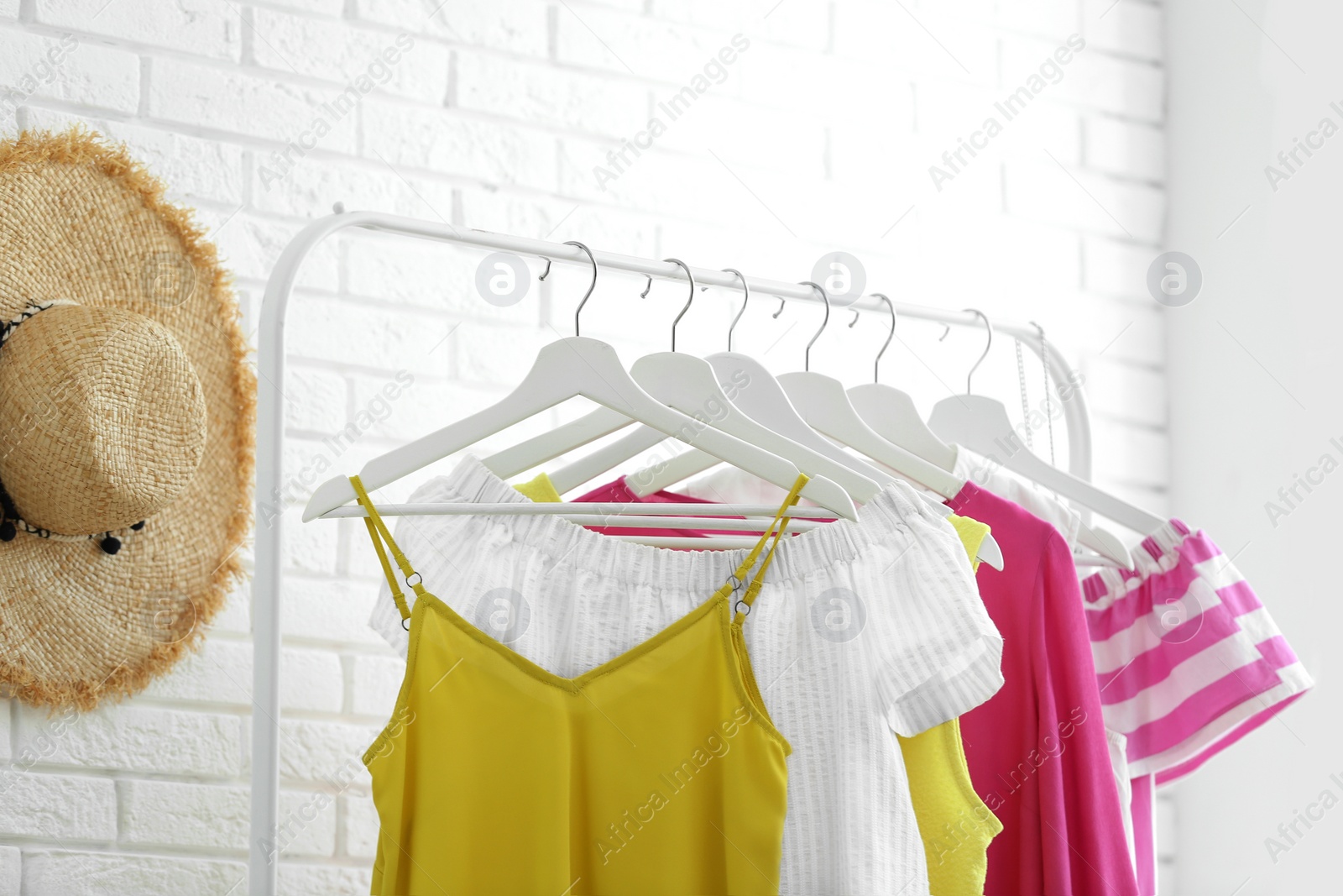 Photo of Wardrobe rack with women's clothes at white brick wall in room