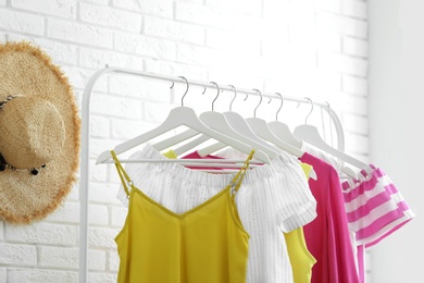 Photo of Wardrobe rack with women's clothes at white brick wall in room