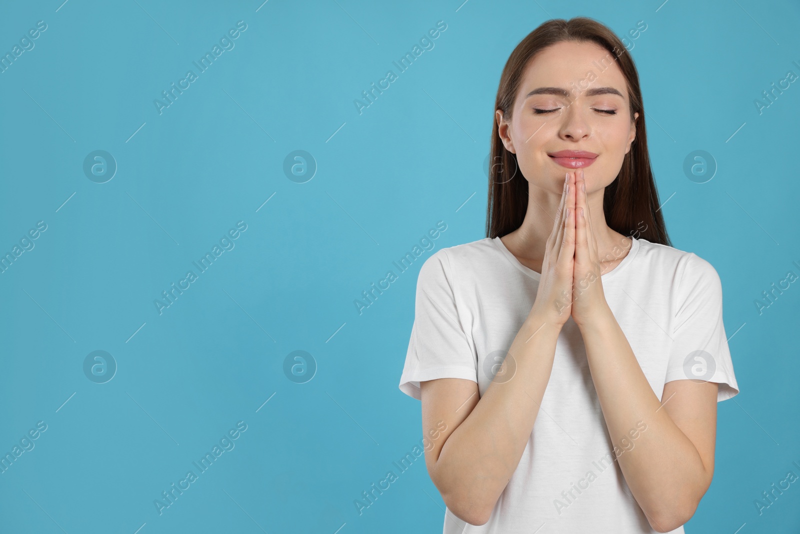 Photo of Woman with clasped hands praying on turquoise background, space for text