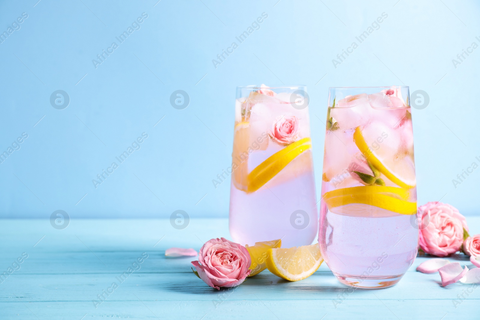 Photo of Tasty refreshing lemon drink with roses on wooden table against light blue background. Space for text