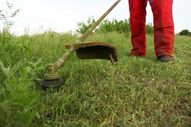 Photo of Worker cutting grass with string trimmer outdoors, closeup view