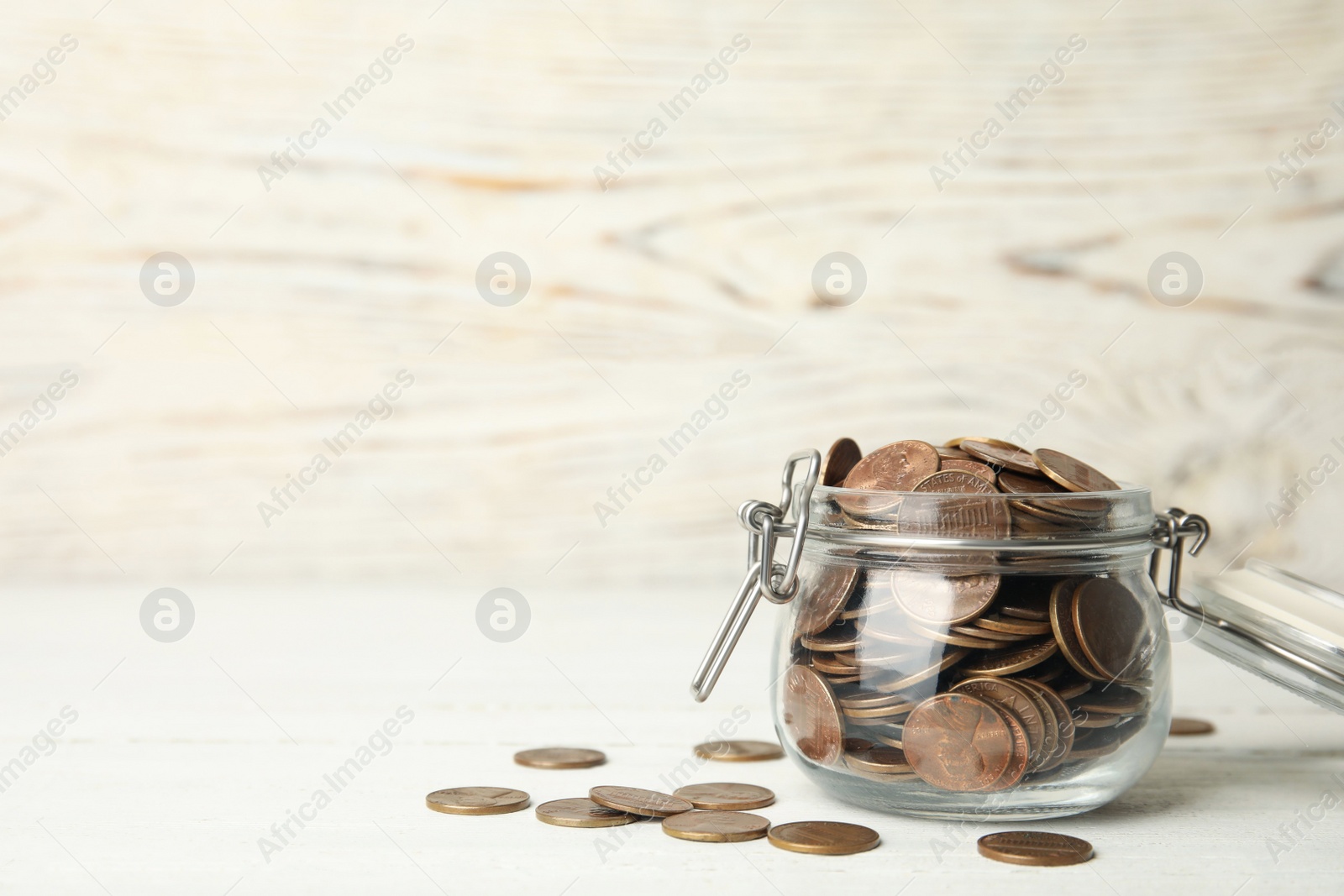 Photo of Glass jar with coins on white wooden table, space for text