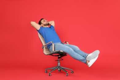 Photo of Young man relaxing in comfortable office chair on red background