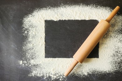 Flour and rolling pin on black table, top view