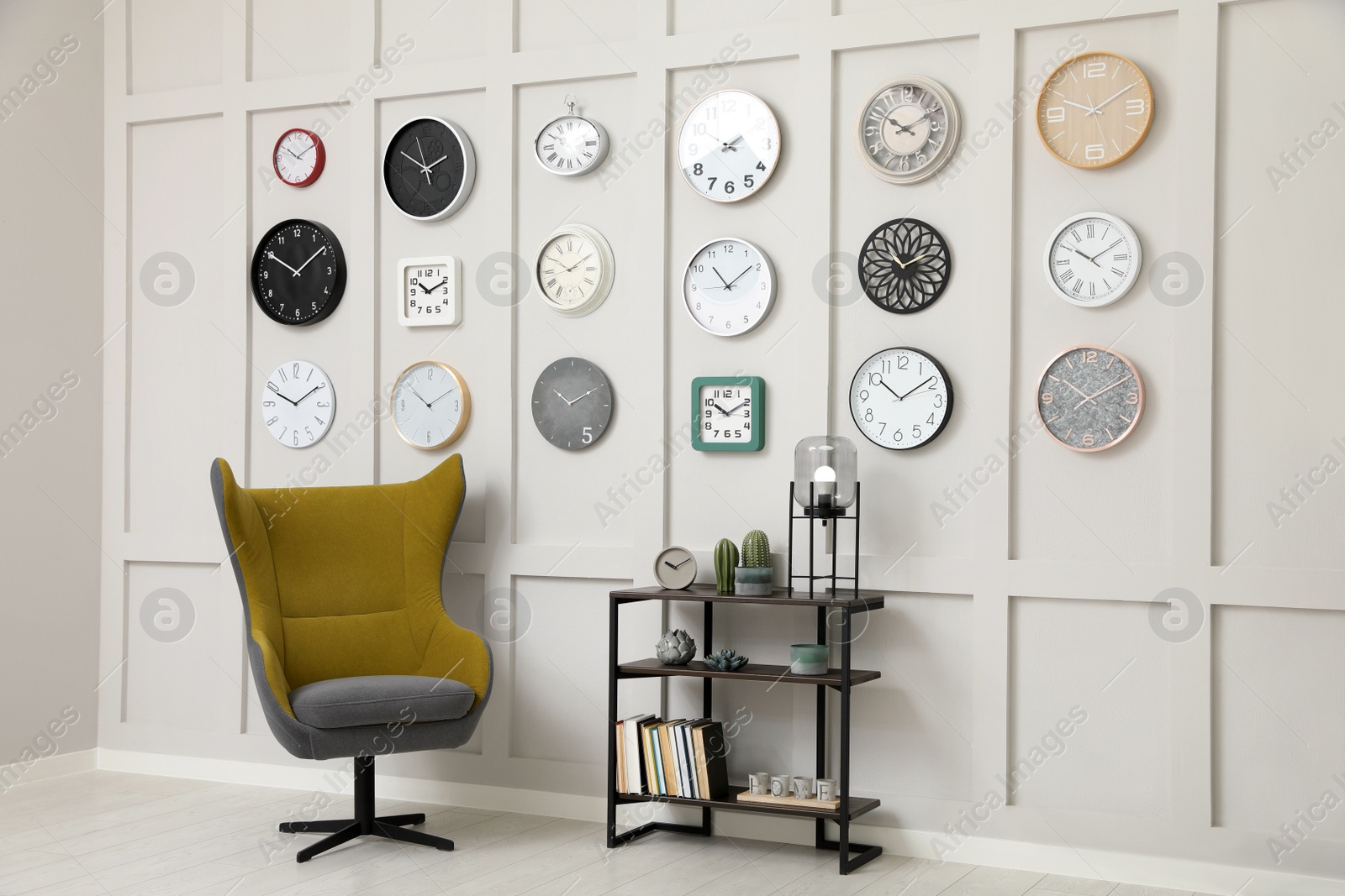 Photo of Armchair, console table and many different clocks hanging on white wall in room