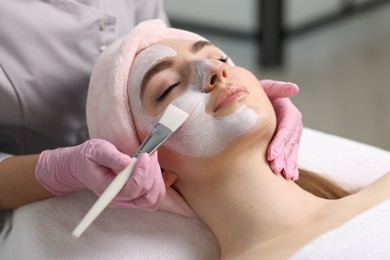 Cosmetologist applying mask on woman's face, closeup