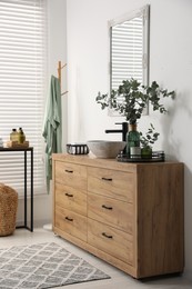 Modern bathroom interior with stylish mirror, eucalyptus branches, vessel sink and wooden vanity