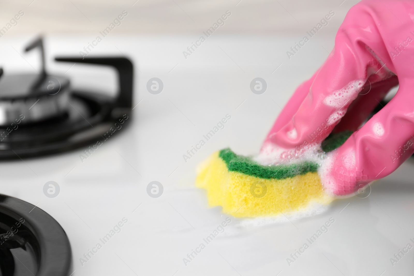 Photo of Person cleaning gas stove with sponge, closeup