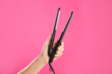 Photo of Woman holding flat hair iron on pink background, closeup