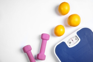 Scales, oranges and dumbbells on white background, top view