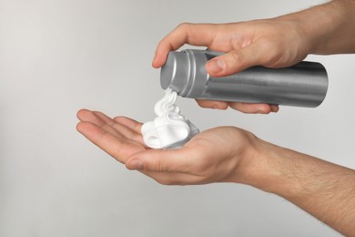 Photo of Man applying shaving foam onto hand on light grey background, closeup