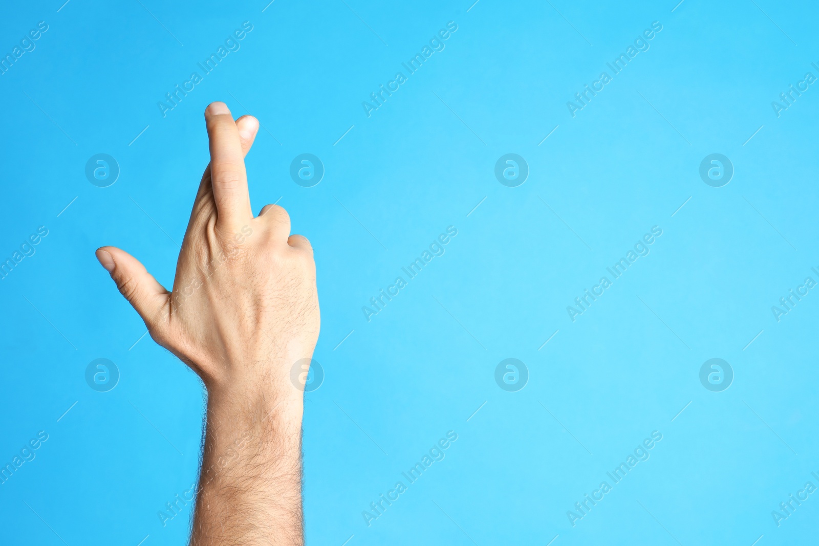 Photo of Man with crossed fingers and space for text on light blue background, closeup. Superstition concept