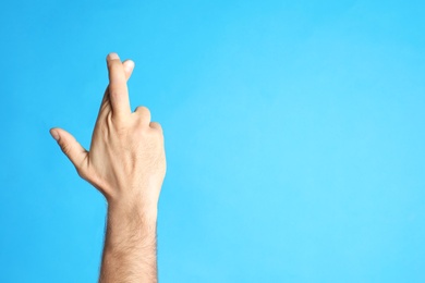 Photo of Man with crossed fingers and space for text on light blue background, closeup. Superstition concept