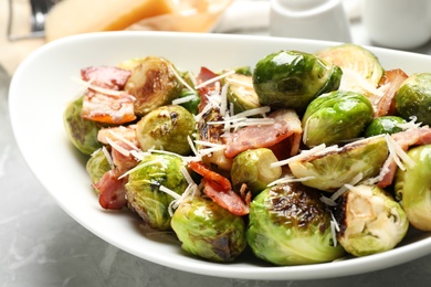 Delicious Brussels sprouts with bacon in plate on light table, closeup