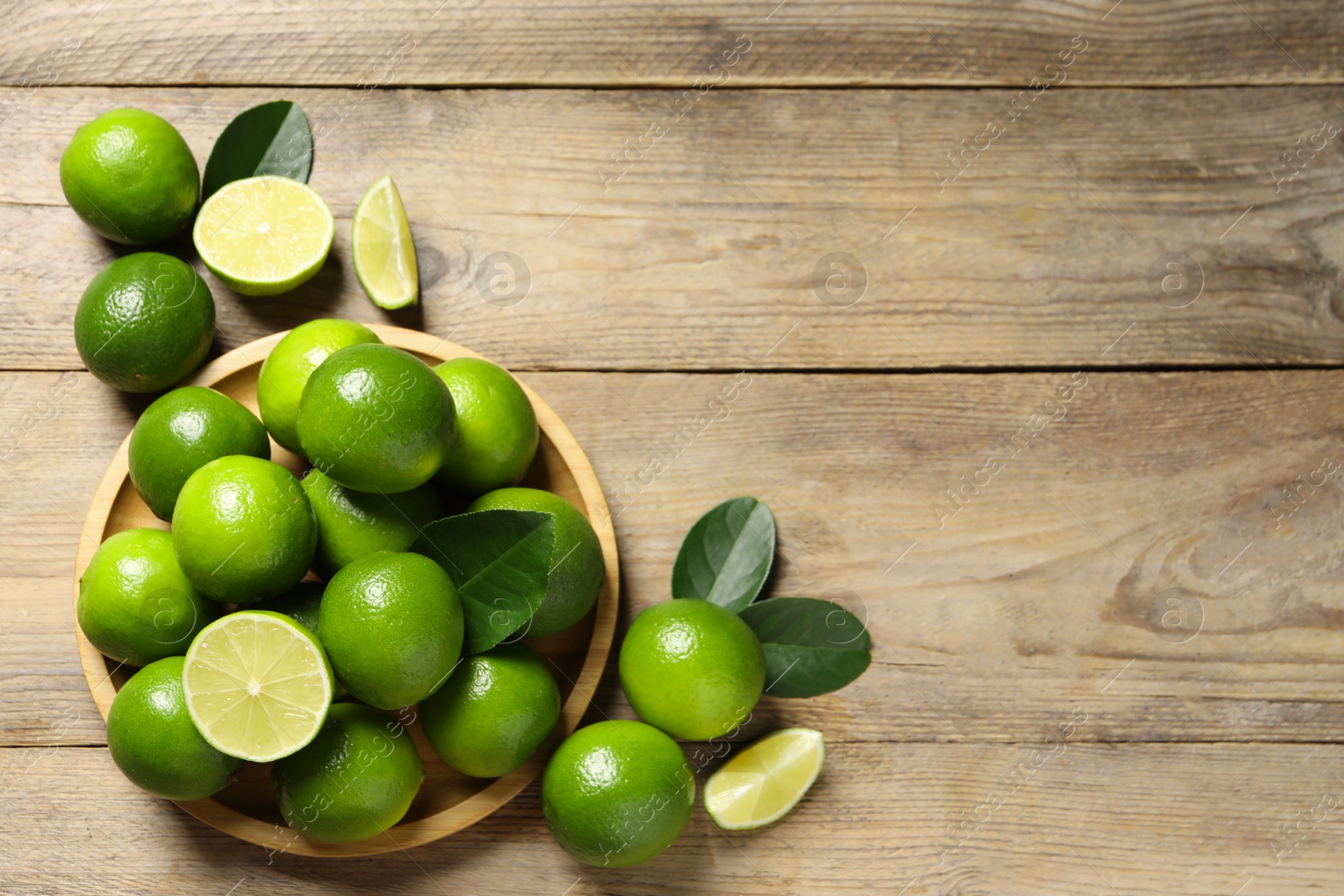 Photo of Fresh limes and green leaves on wooden table, flat lay. Space for text