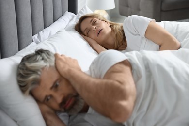 Photo of Irritated man covering his ears in bed at home Problem with snoring wife