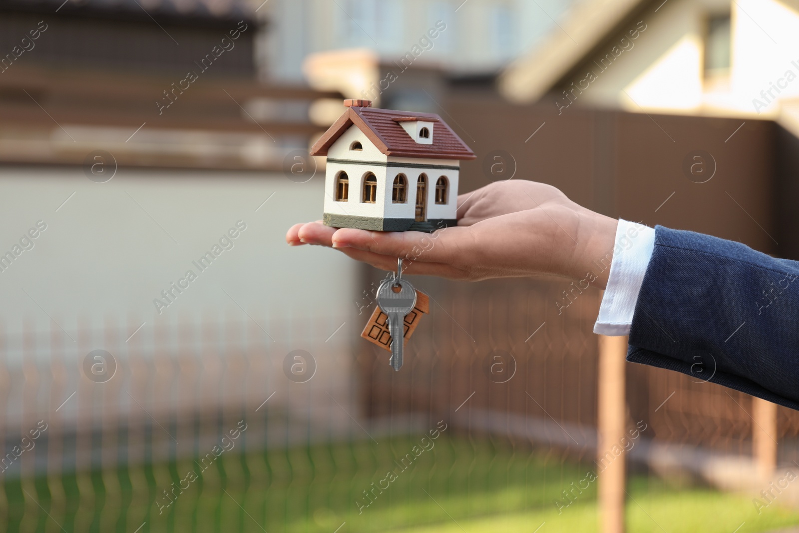 Photo of Real estate agent holding key and house model outdoors, closeup