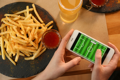 Photo of Woman playing game using smartphone at table with tasty snacks, top view