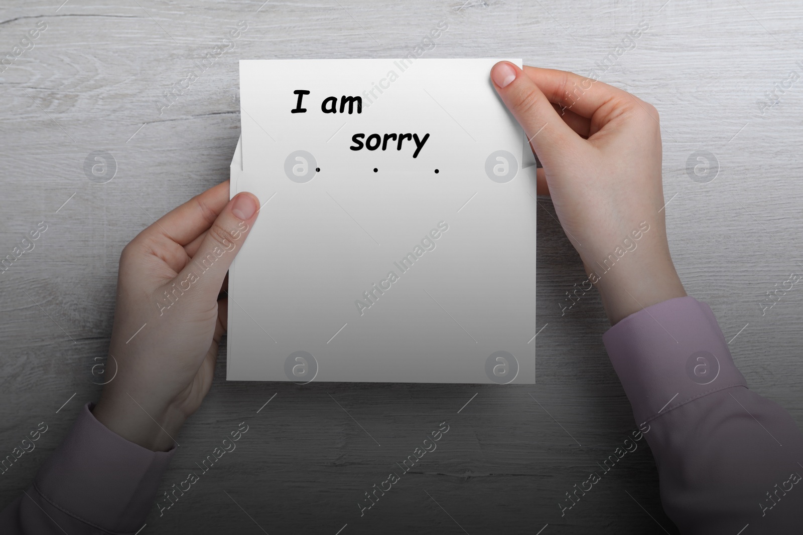Image of Apology. Woman taking card with phrase I Am Sorry out of envelope at wooden table, top view