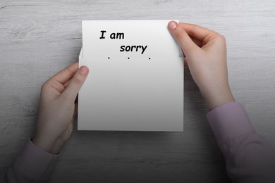 Apology. Woman taking card with phrase I Am Sorry out of envelope at wooden table, top view