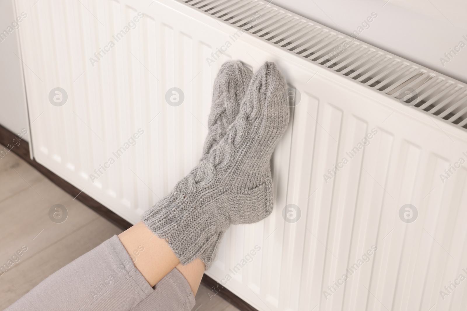 Photo of Woman warming feet near heating radiator indoors, closeup