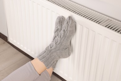 Woman warming feet near heating radiator indoors, closeup