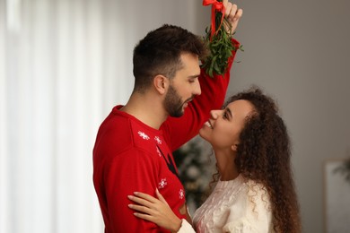 Photo of Lovely couple under mistletoe bunch in room. Christmas time