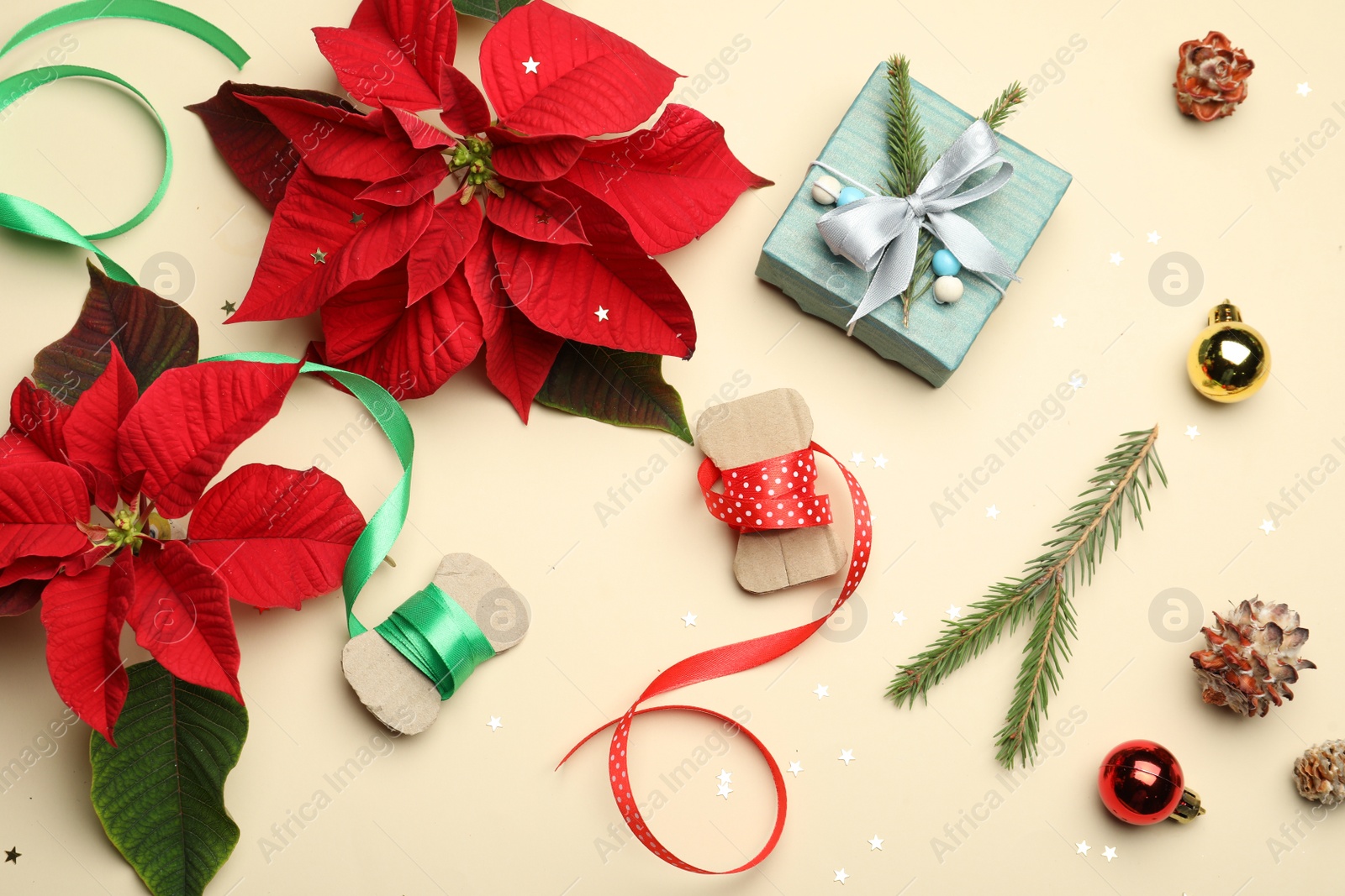 Photo of Flat lay composition with poinsettias (traditional Christmas flowers) and holiday decor on beige background