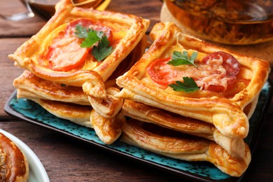 Fresh delicious puff pastry with cheese, tomatoes and parsley on wooden table, closeup