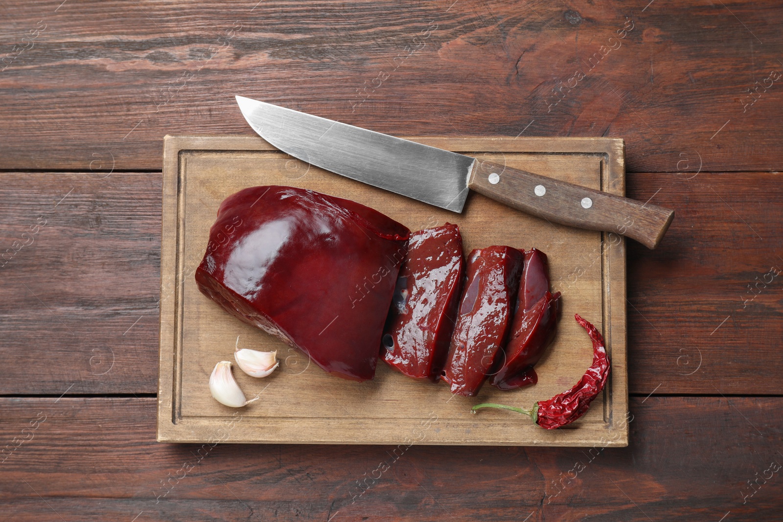 Photo of Cut raw beef liver with chili pepper, garlic and knife on wooden table, top view