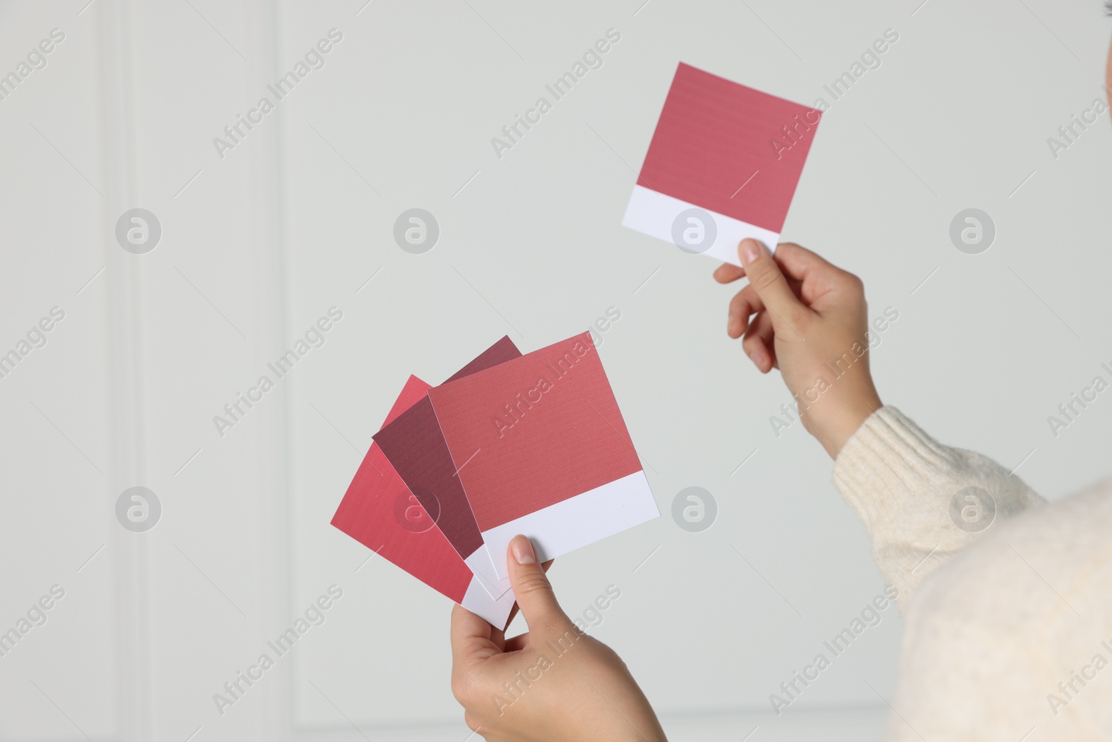 Photo of Woman with color sample cards choosing paint shade for wall indoors, closeup. Interior design