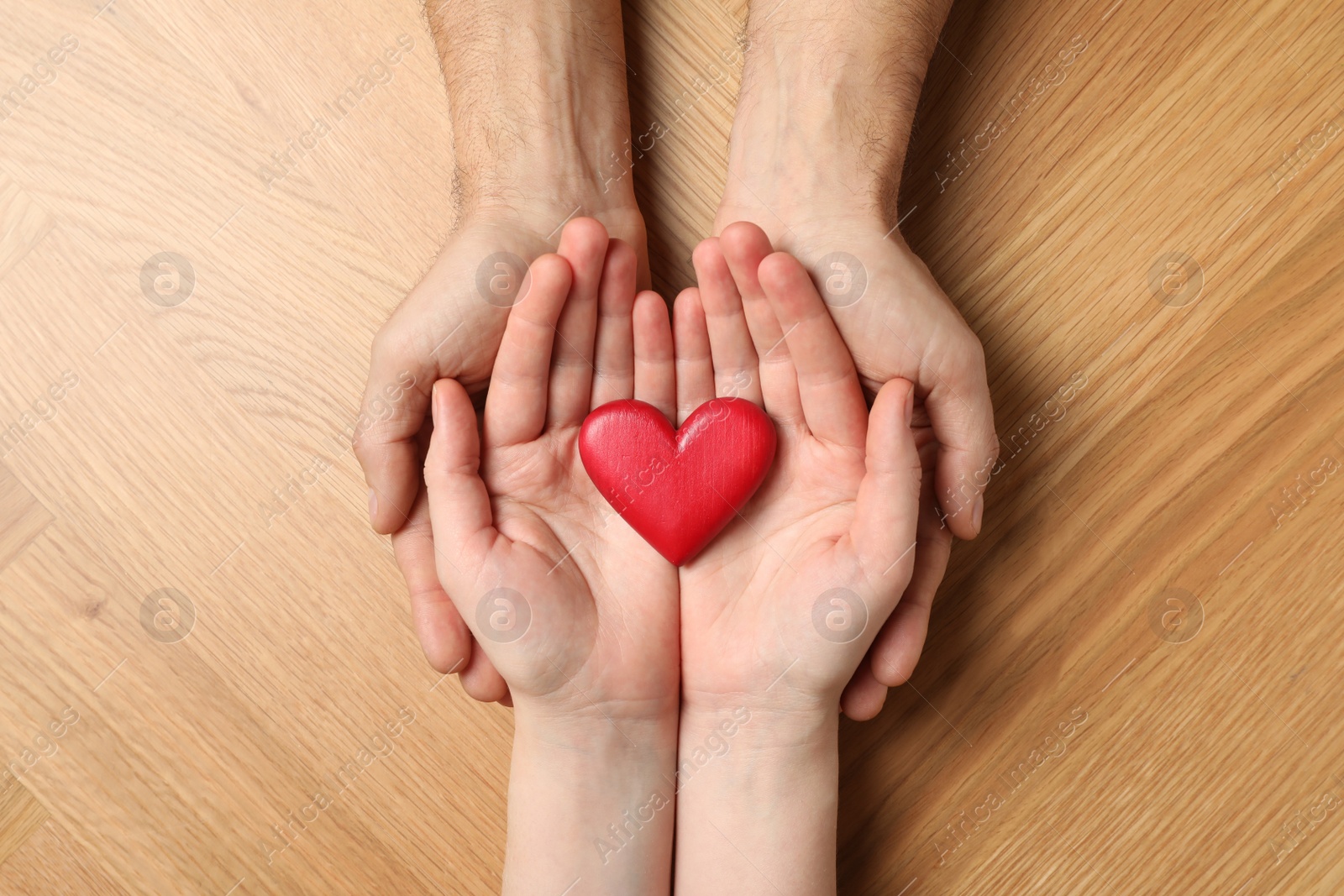 Photo of Couple holding red heart in hands at wooden table, top view