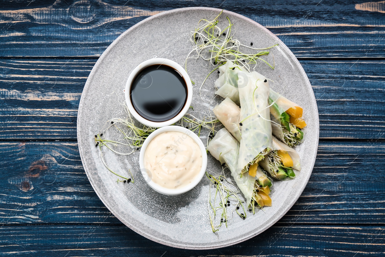 Photo of Delicious rolls wrapped in rice paper served on blue wooden table, top view