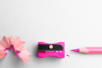 Photo of Pink pencil, sharpener and shavings on white background, flat lay. Space for text
