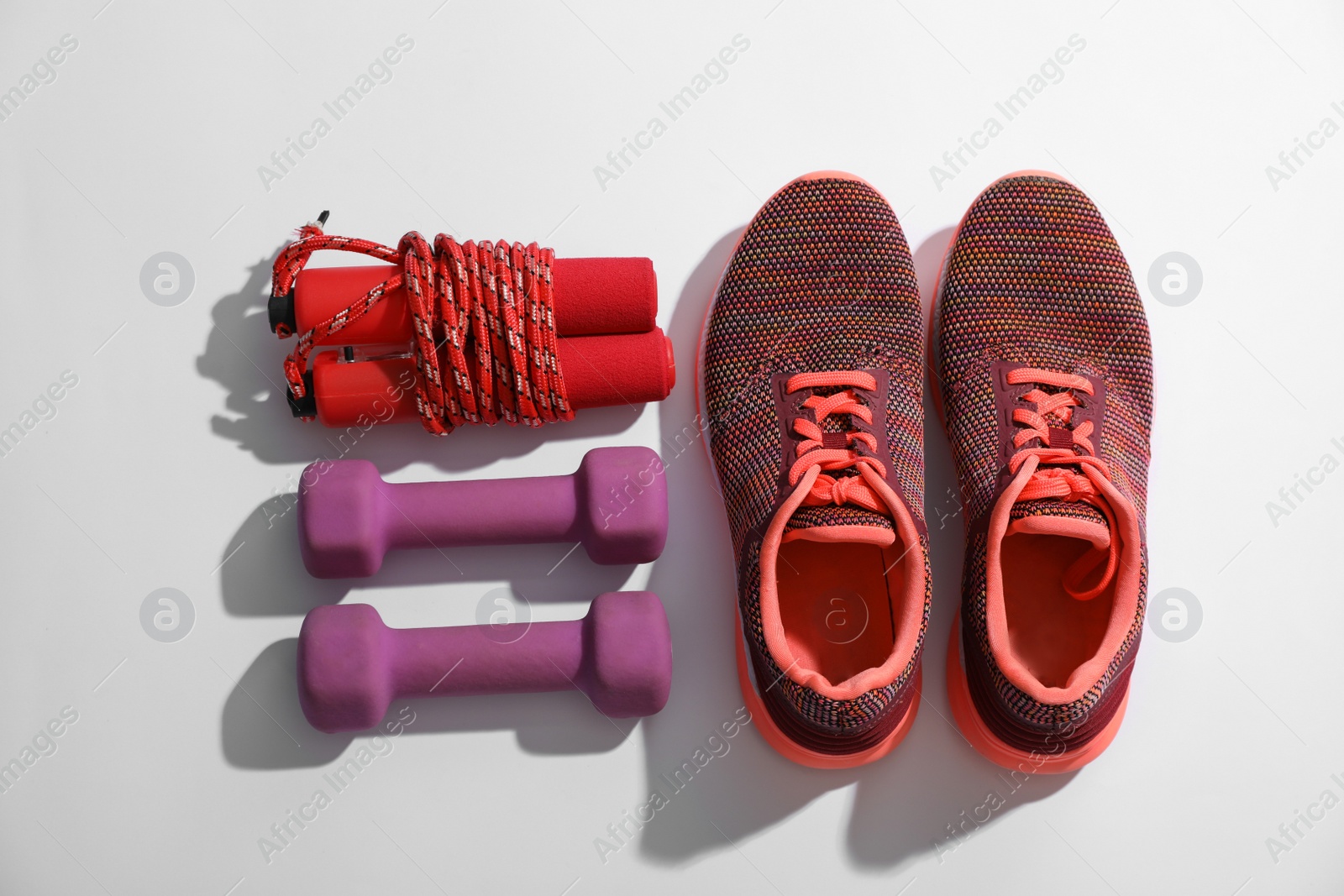 Photo of Sneakers, dumbbells and skipping rope on white background, top view. Physical fitness