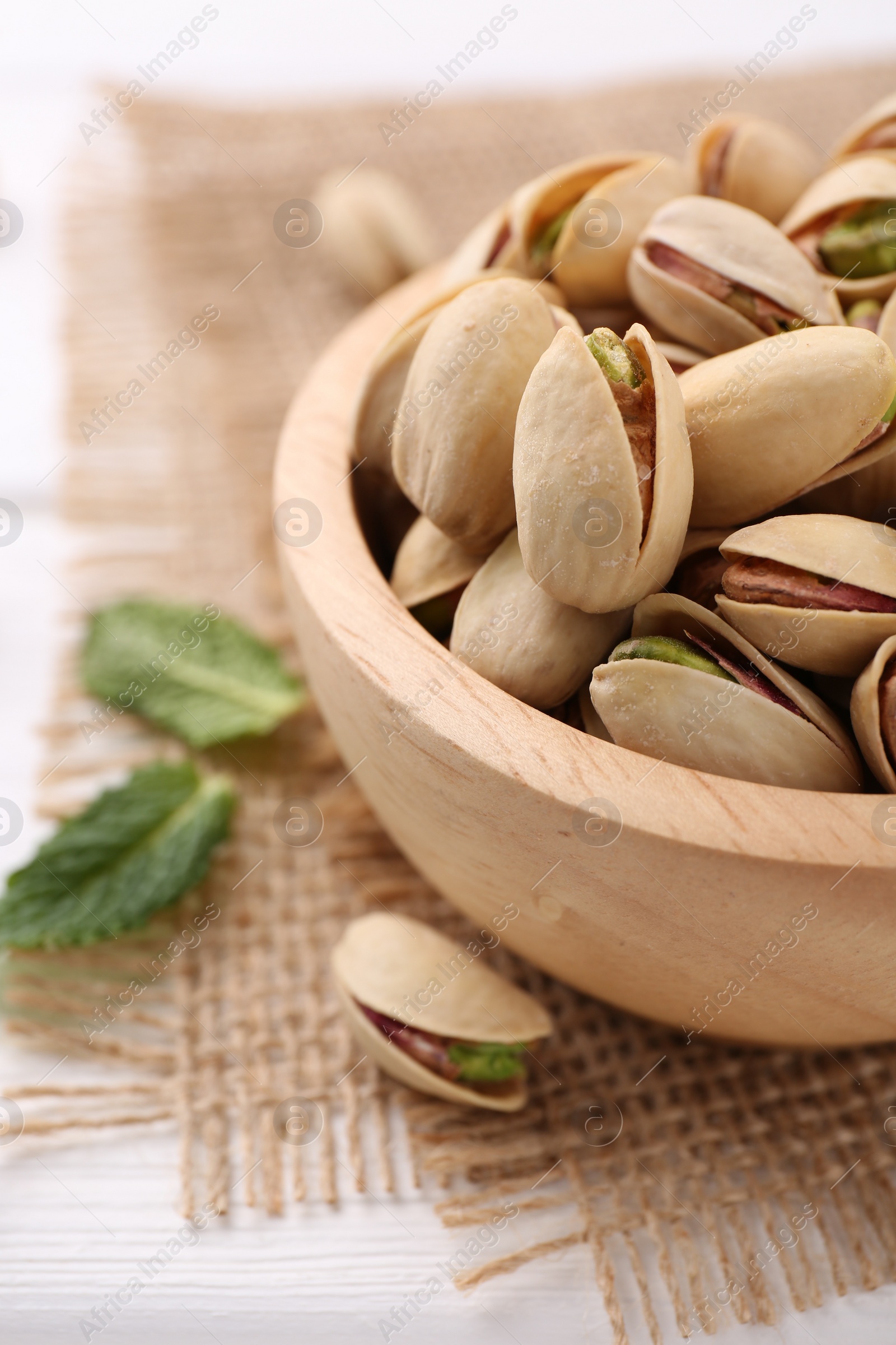 Photo of Tasty pistachios in bowl on white wooden table, closeup