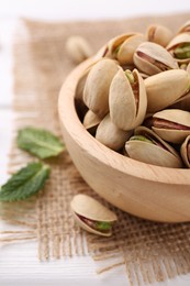 Tasty pistachios in bowl on white wooden table, closeup