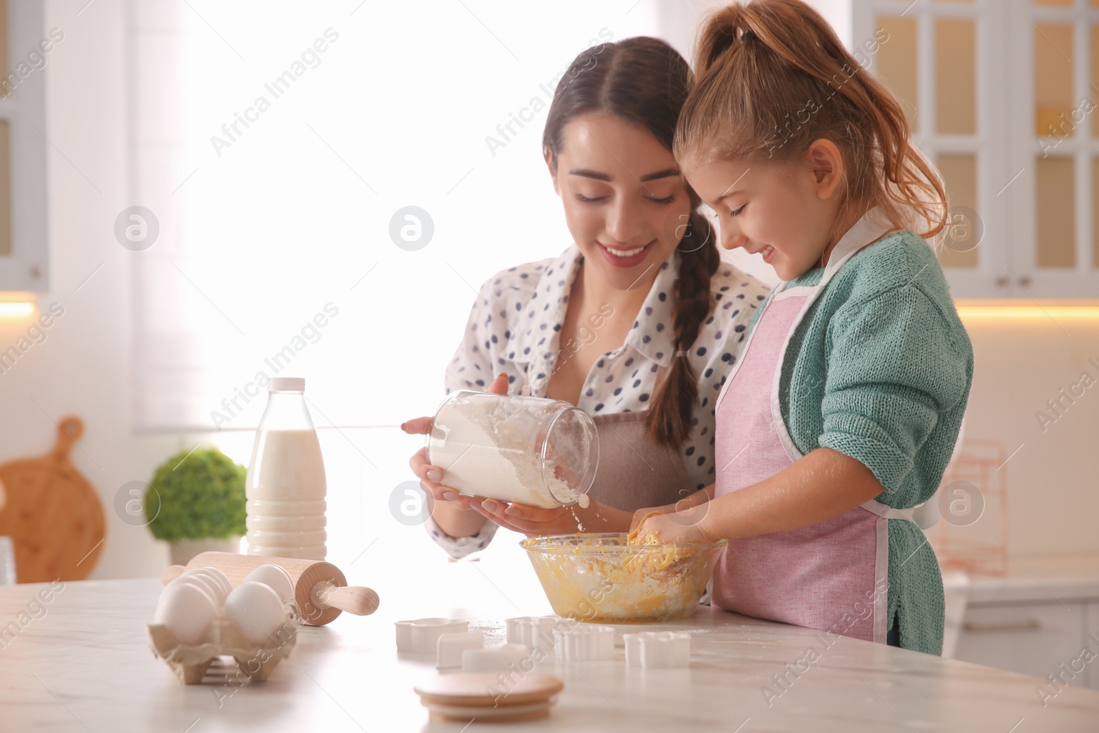 Photo of Mother and daughter making dough at table in kitchen