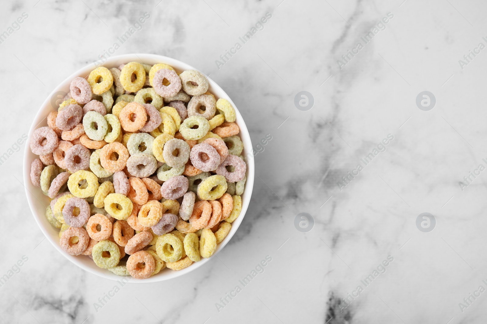 Photo of Tasty cereal rings in bowl on white marble table, top view. Space for text