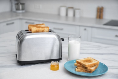 Photo of Modern toaster with slices of bread, honey and milk on white marble table in kitchen