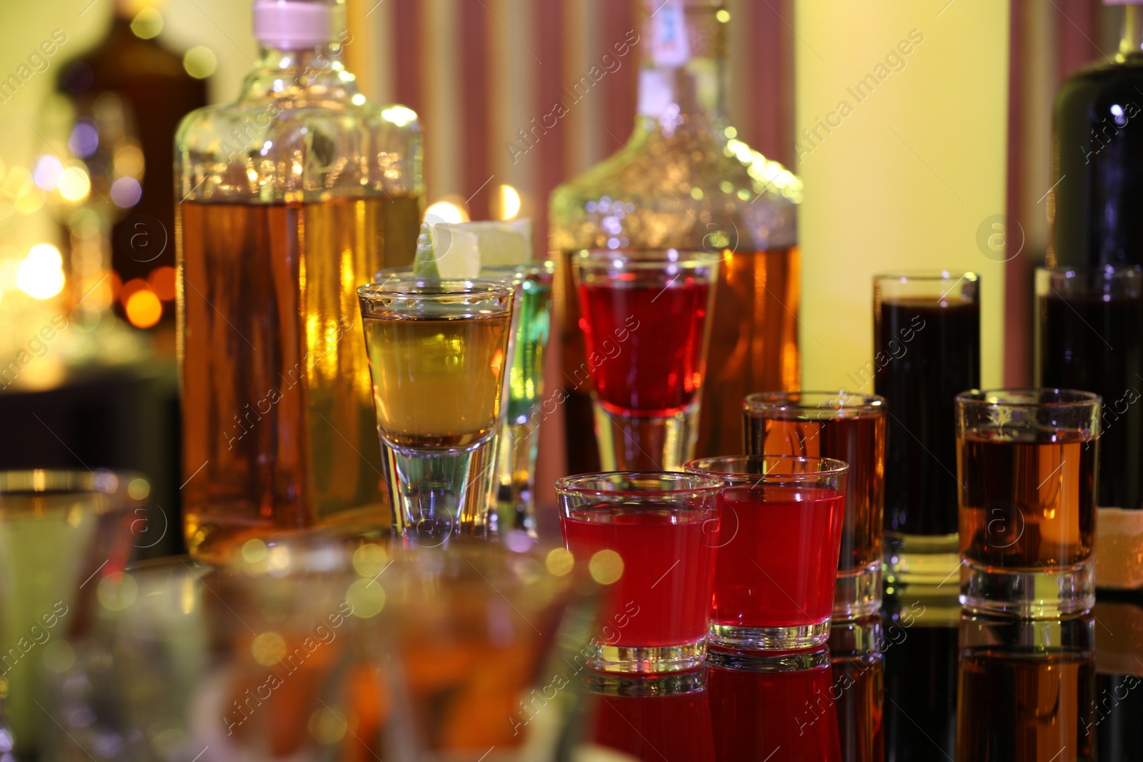 Photo of Different shooters in shot glasses and bottles on mirror surface. Alcohol drink