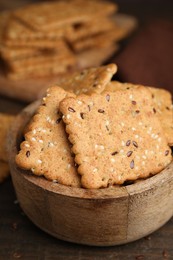 Photo of Cereal crackers with flax and sesame seeds in bowl on wooden table, closeup