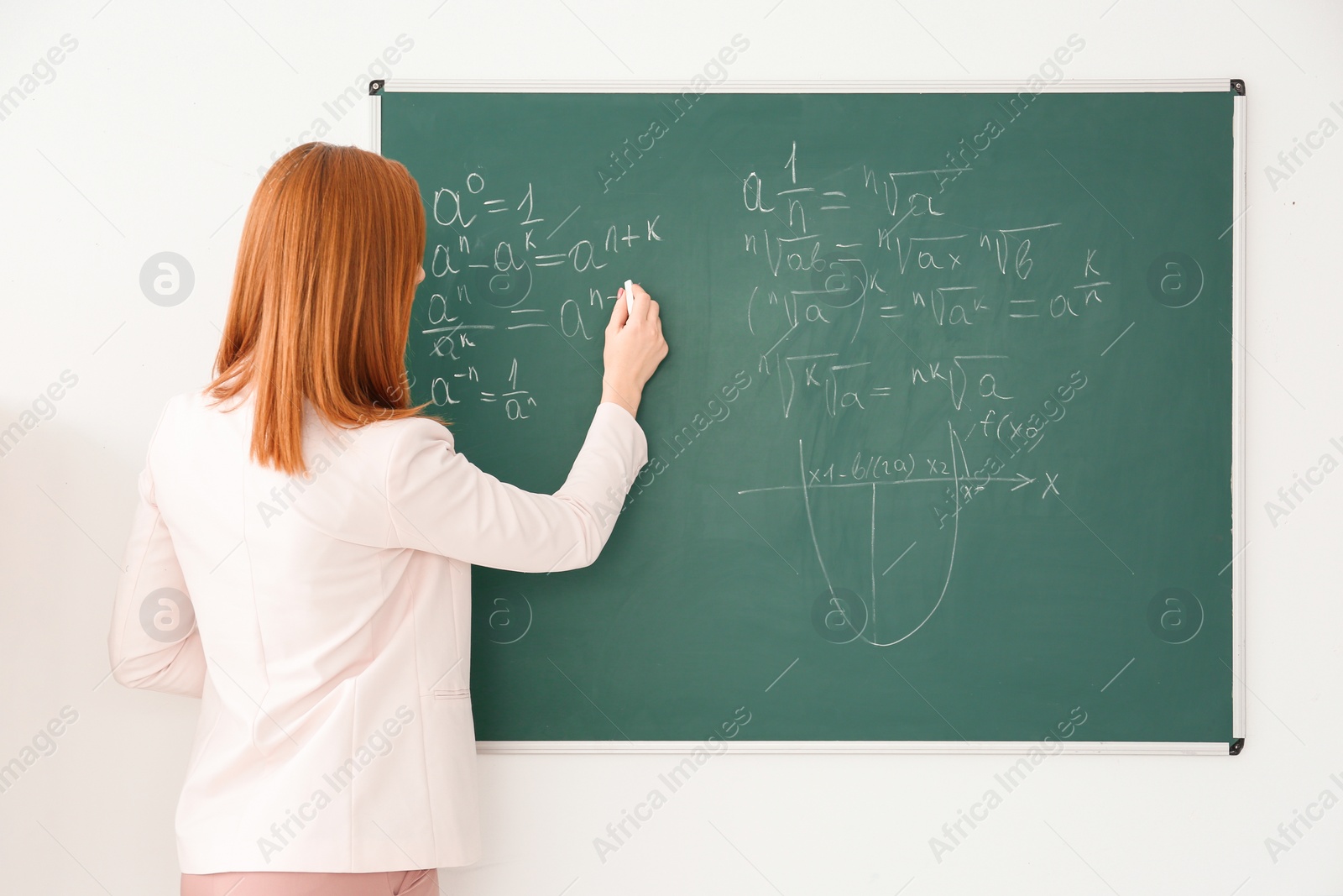 Photo of Beautiful young teacher writing on blackboard in classroom