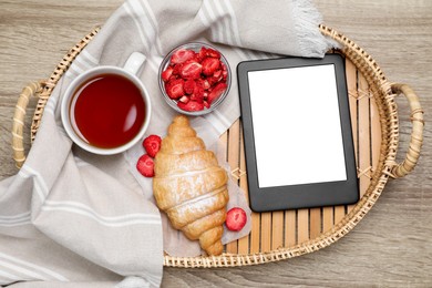 Tray with e-book reader and breakfast on wooden table, top view. Space for text