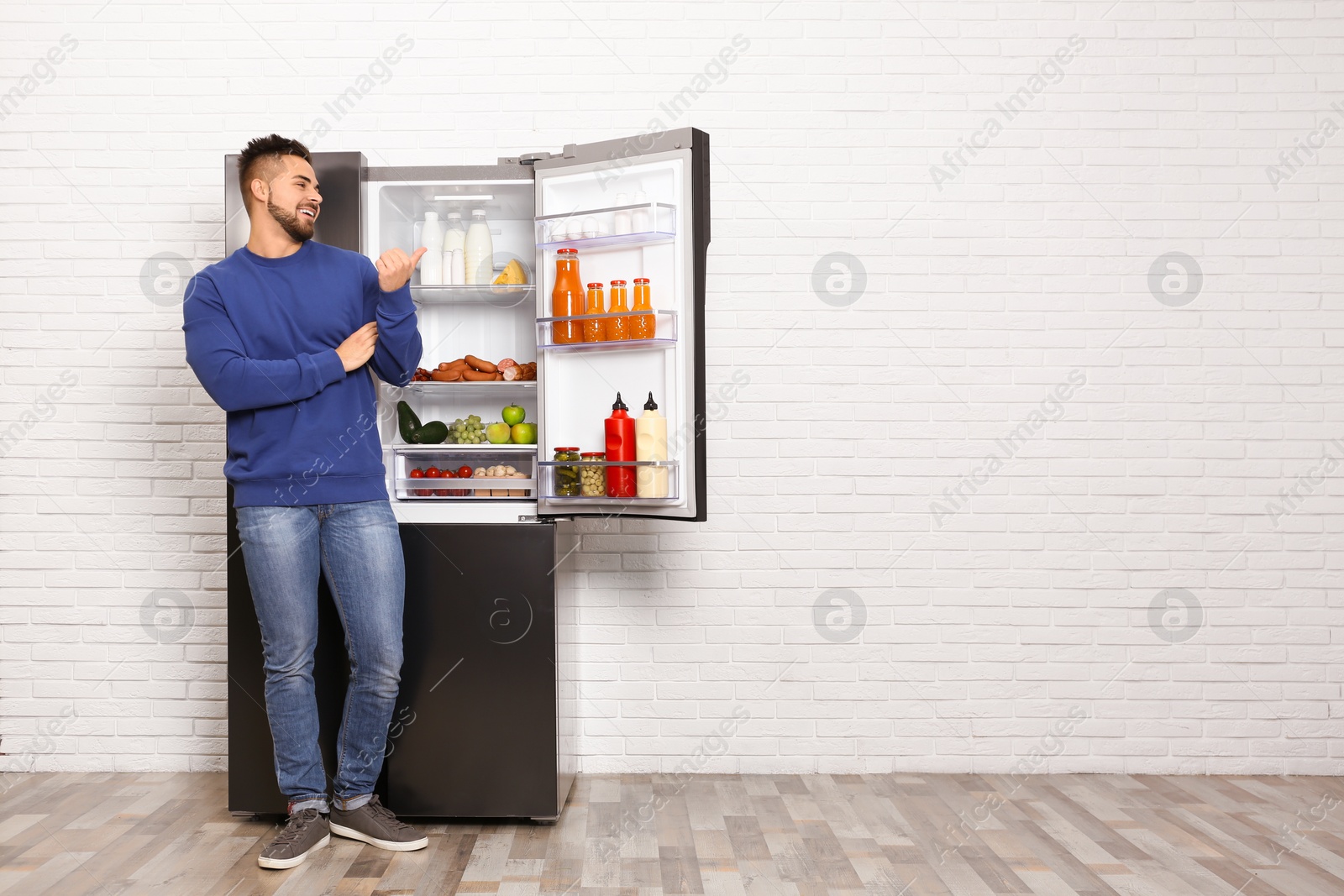 Photo of Happy young man near open refrigerator indoors, space for text