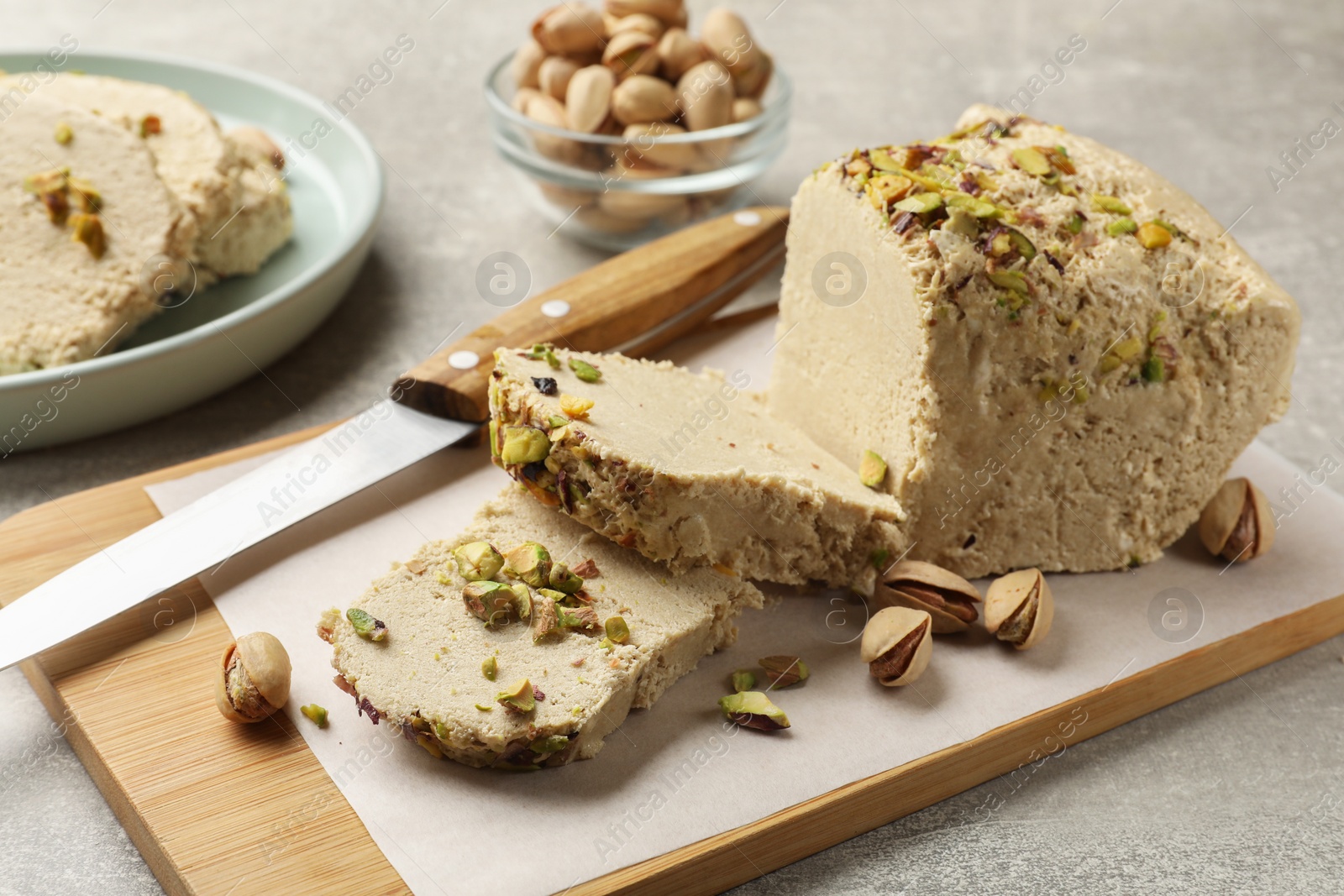 Photo of Tasty halva with pistachios and knife on grey table, closeup