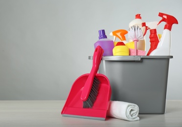 Photo of Bucket with different cleaning products and supplies on light table. Space for text