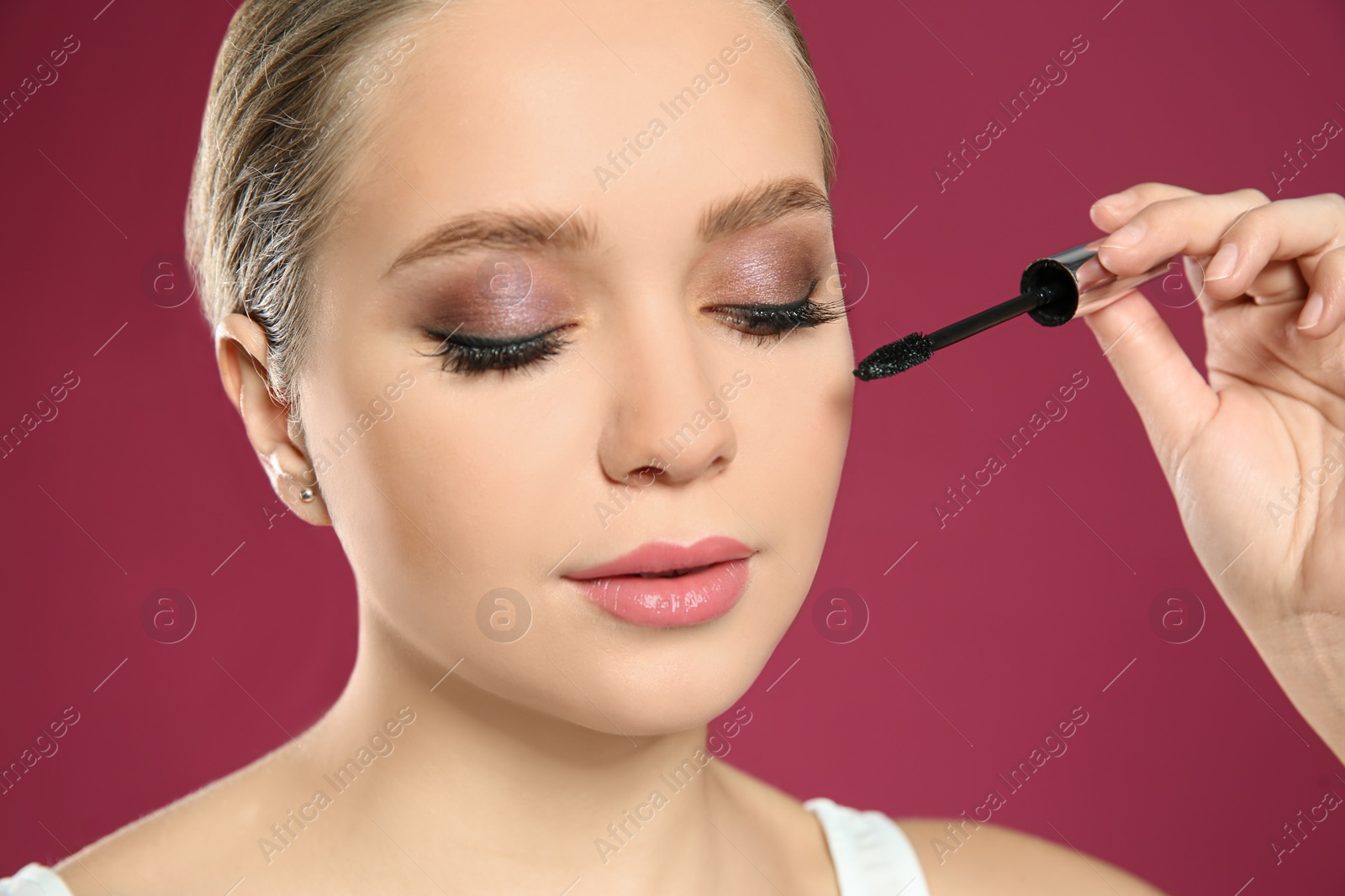 Photo of Beautiful woman applying mascara on pink background, closeup. Stylish makeup