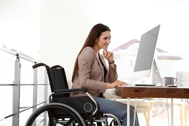 Young woman in wheelchair using computer at workplace